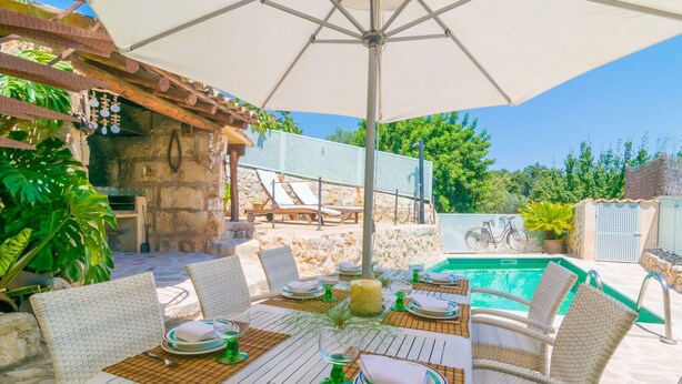 An outdoor dining area with wicker chairs and tables, a pool, and a stone wall in the background.