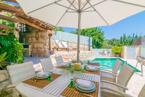 Un área de comedor al aire libre con sillas y mesas de mimbre, una piscina y un muro de piedra al fondo.