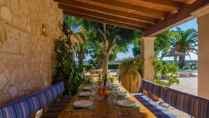 Un'area pranzo all'aperto riparata, con un muro in pietra, panche di legno e vista sulla spiaggia.