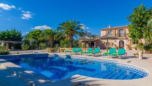 Una piscina con lettini, un edificio con finestre ad arco e palme.