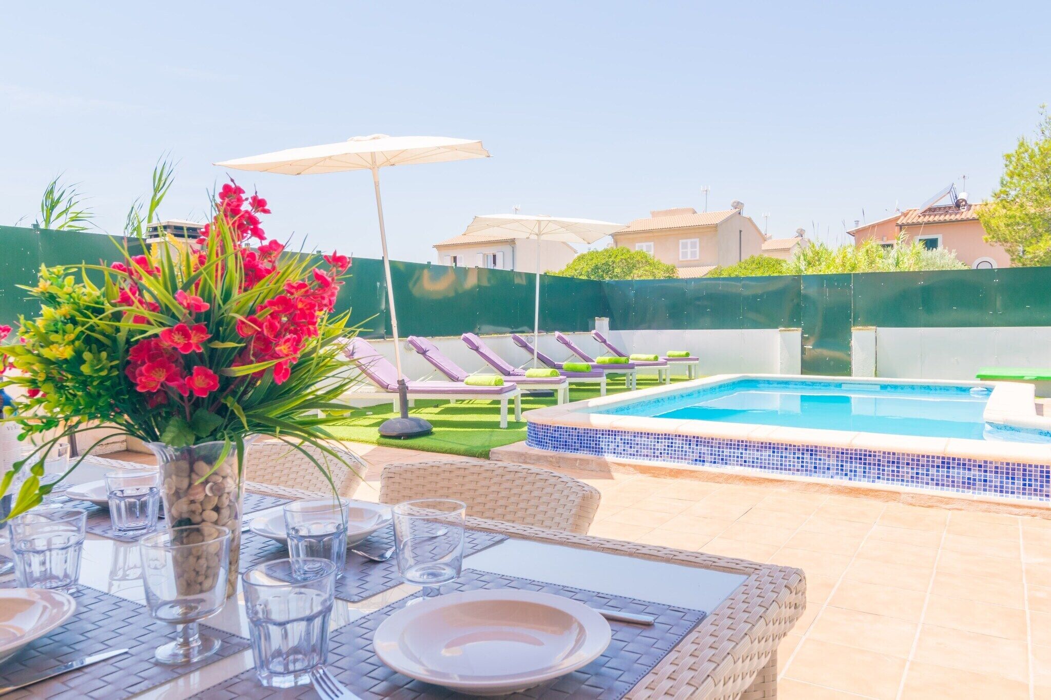 A poolside area with lounge chairs, a dining table set with plates and glasses, and a flower vase.