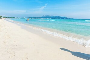 A beach with clear turquoise water, a sandy shore, and a mountain in the background.
