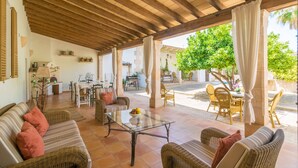 Un patio cubierto con muebles de mimbre, una mesa de centro de vidrio y vistas a la calle y la vegetación circundante.
