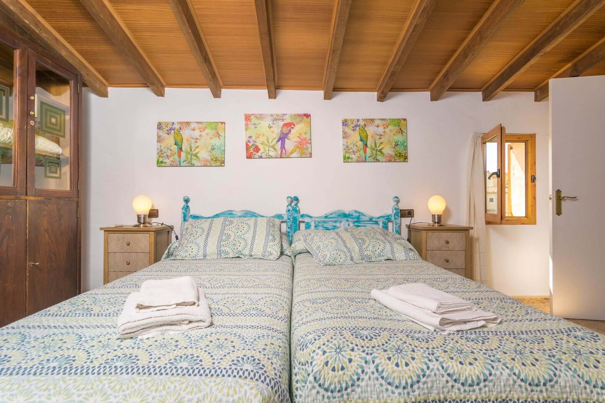 A double bed with patterned bedding, two bedside tables with lamps, and a wooden wardrobe.