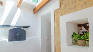 A room with a white wall, a stone accent wall, a window with a plant, and a black object on the wall. - Sa Rota (den Joan Porrerenc) - Apartment (MontuÏri, Illes Balears)