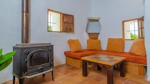 A cozy room with a wood-burning stove, a sofa with cushions, a table, and a window with a view. - Sa Rota (den Joan Porrerenc) - Apartment (MontuÏri, Illes Balears)
