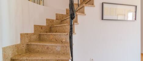 A staircase with a wooden handrail and beige steps, leading to a landing with a framed picture and two wall-mounted lanterns.