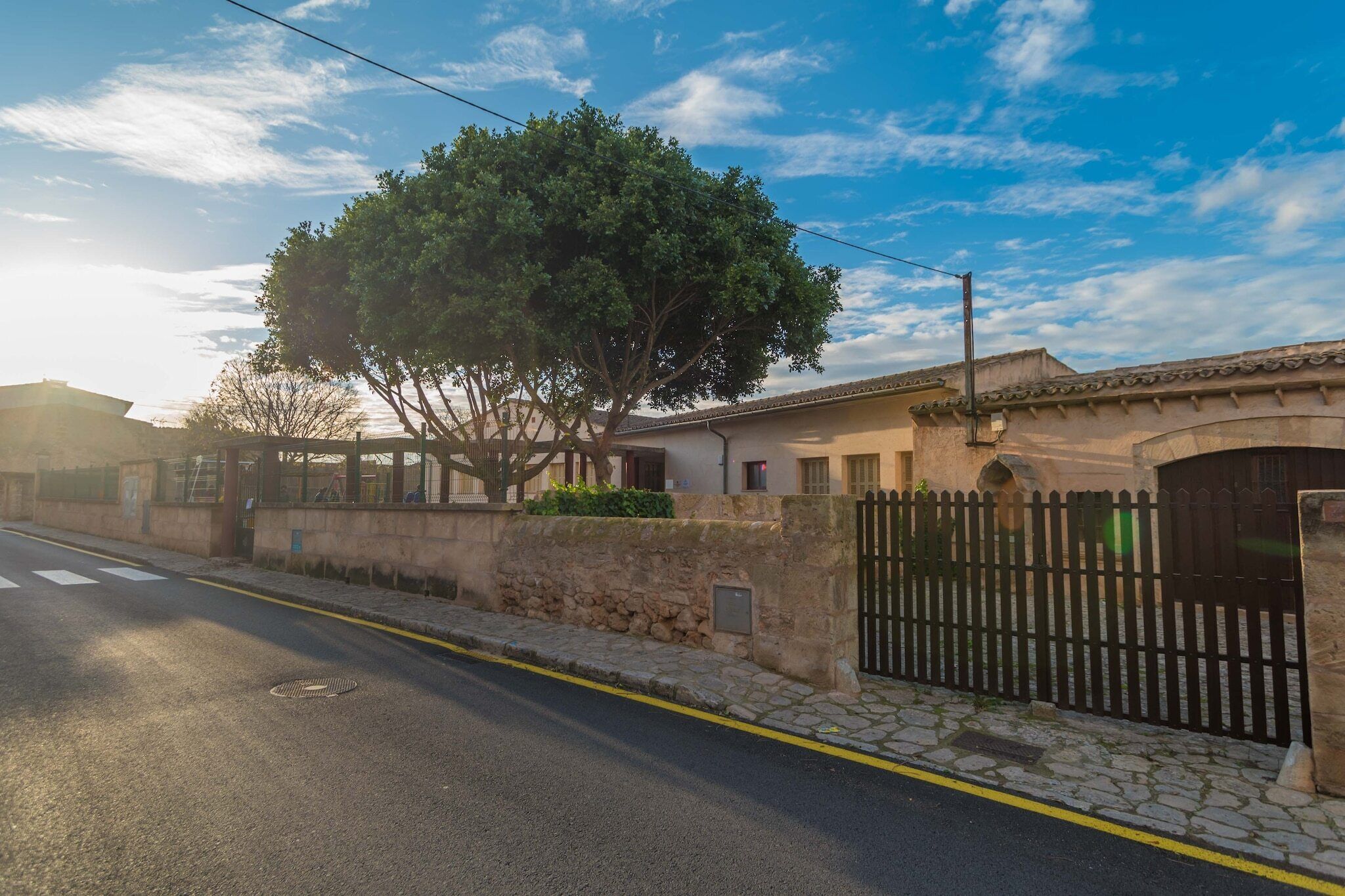 A street view with a house, a tree, and a stone wall.