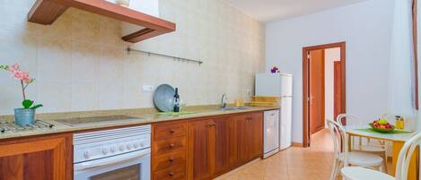 A kitchen with wooden cabinets, a built-in oven, a sink, and a dining area with a table and chairs.