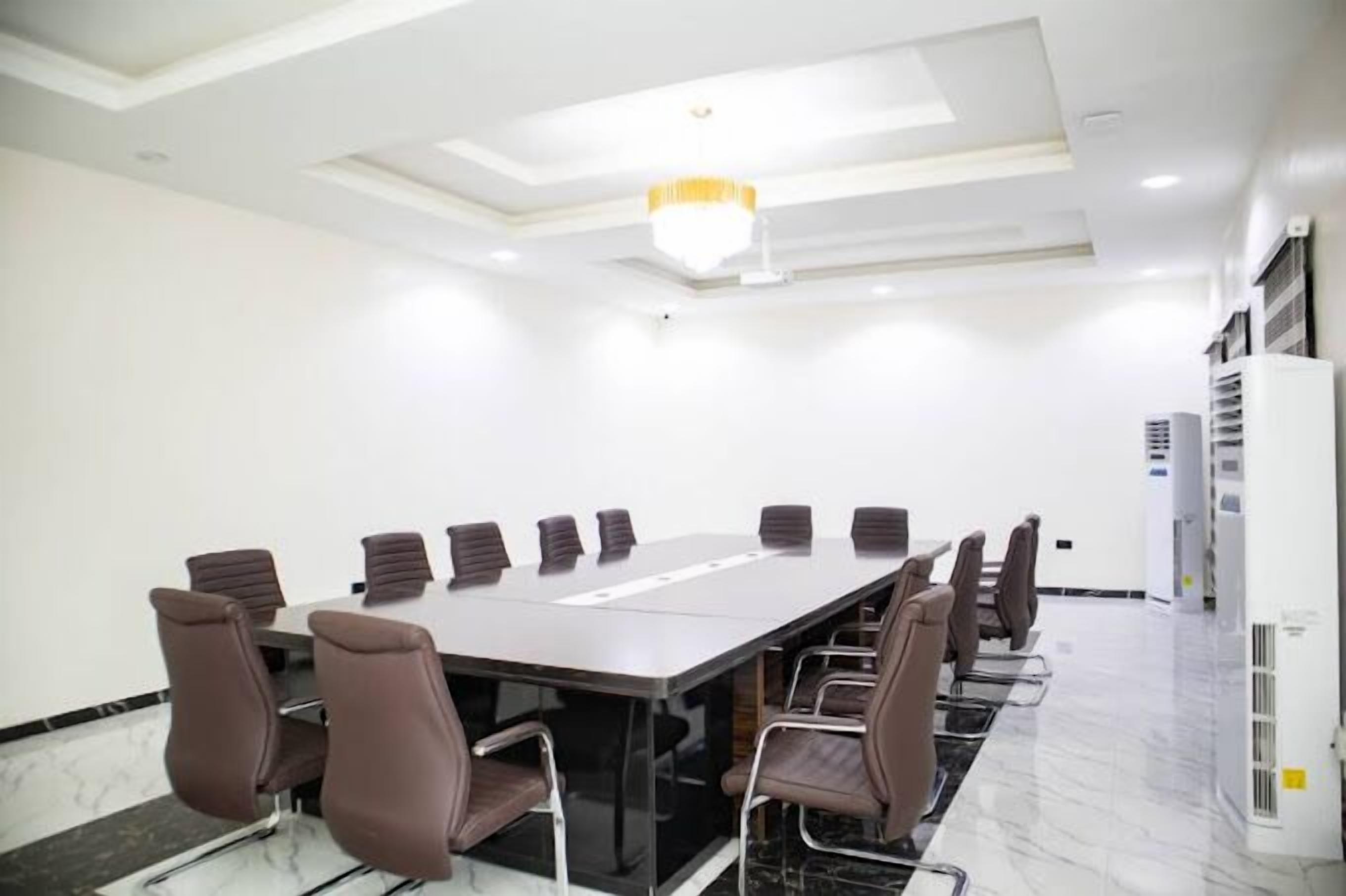 Une salle de conférence avec une longue table et des chaises, des murs blancs et un lustre.