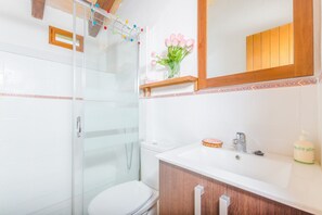 Une salle de bain moderne avec une douche à parois de verre, des toilettes blanches et un meuble-lavabo en bois surmonté d’un miroir.