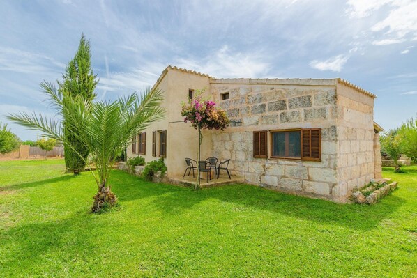 Une maison en pierre avec un petit patio, un palmier et une composition florale.