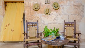Una habitación rústica con una mesa de madera, dos sillas, una cortina amarilla y tres sombreros en la pared.