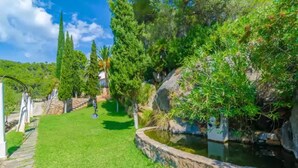 A well-maintained garden with a stone pathway leading to a pond, surrounded by various trees and shrubs. - Can Bolei - Villa With Private Pool In Sant Elm (Sant Elm (andratx), Illes Balears)
