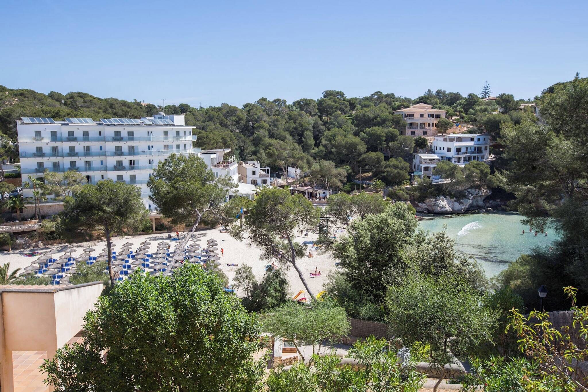 Un hôtel situé sur la côte, avec plusieurs étages, une plage équipée de parasols et un rivage rocheux.