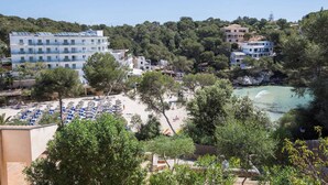 A coastal hotel with multiple floors, a beach area with umbrellas, and a rocky shoreline. - Xalet S'escaleta - Villa With Private Pool (Cala Santanyí, Illes Balears)