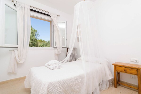 A bedroom with a bed, a bedside table, and a window with curtains.