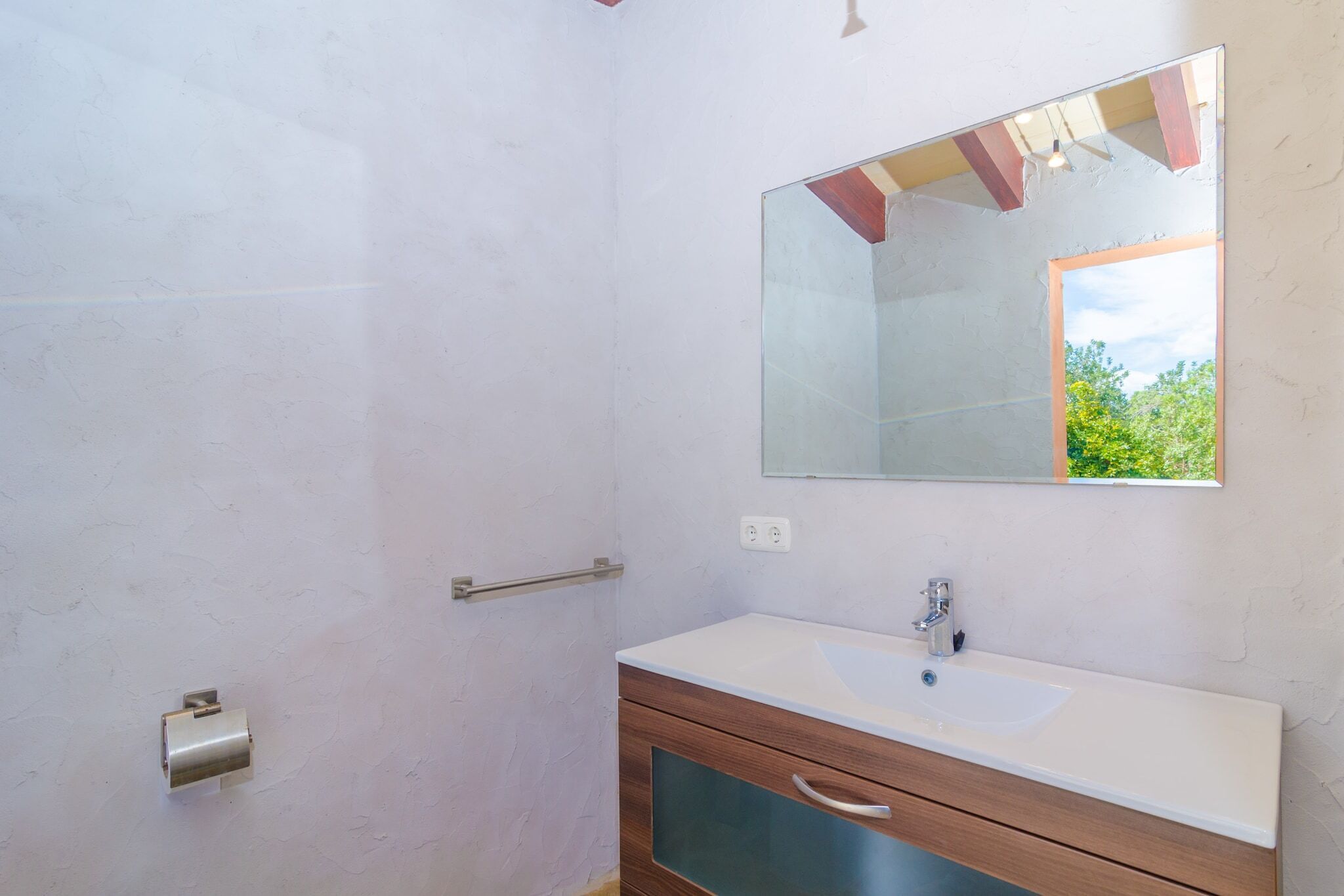 Un baño con lavamanos blanco, tocador de madera y un espejo grande.