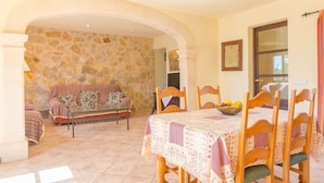 A dining area with a stone wall, a sofa, and a table set with chairs and a fruit bowl. - S'alqueria - Villa With Private Pool In Campanet (Campanet, Illes Balears)