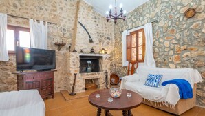 A stone-walled room with a fireplace, a television, a sofa, and a coffee table. - Finca Can Calisto - Apartment With Private Pool (Inca, Illes Balears)