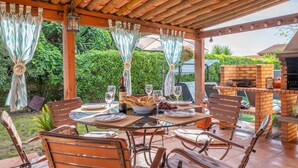 An outdoor patio with a brick barbecue, wooden tables and chairs, and a pergola with curtains. - Finca Can Calisto - Apartment With Private Pool (Inca, Illes Balears)