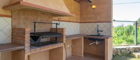 An outdoor kitchen with a brick oven, a sink, and a pergola structure.