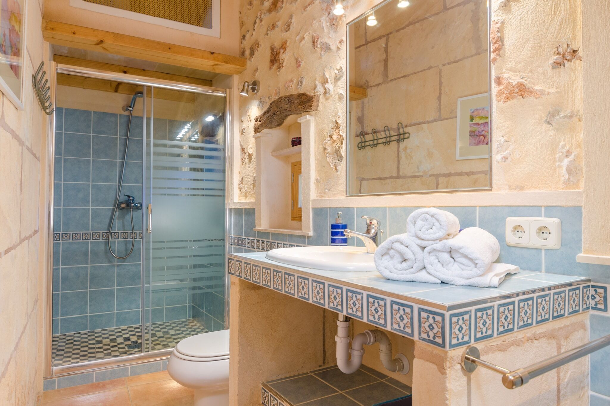 Un baño con cabina de ducha de vidrio, un lavamanos blanco con un borde de azulejos decorativos y un espejo sobre el lavamanos.