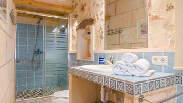 Un baño con cabina de ducha de vidrio, un lavamanos blanco con un borde de azulejos decorativos y un espejo sobre el lavamanos.