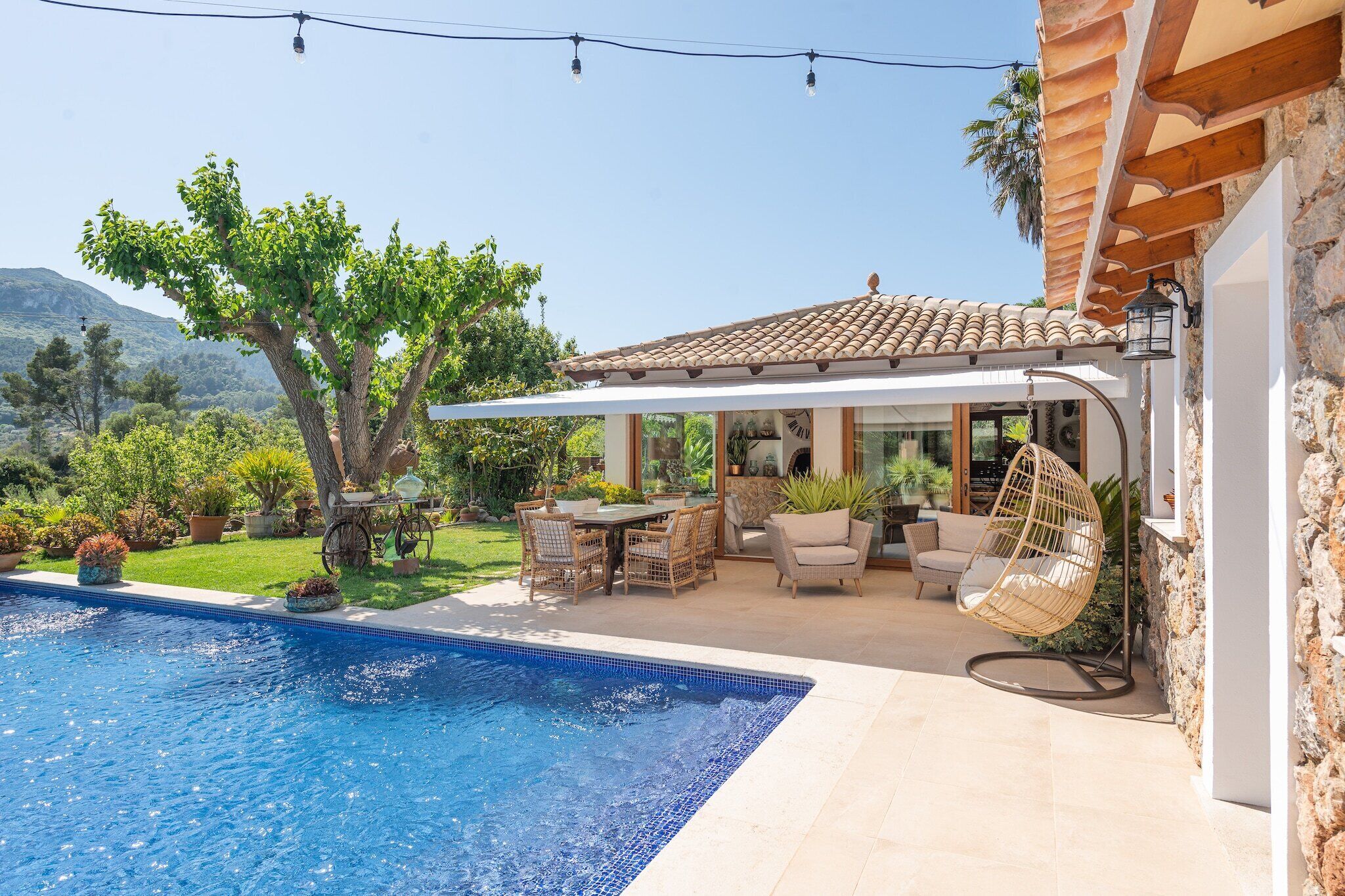 Un área junto a la piscina con una pérgola, muebles de exterior y una silla colgante.
