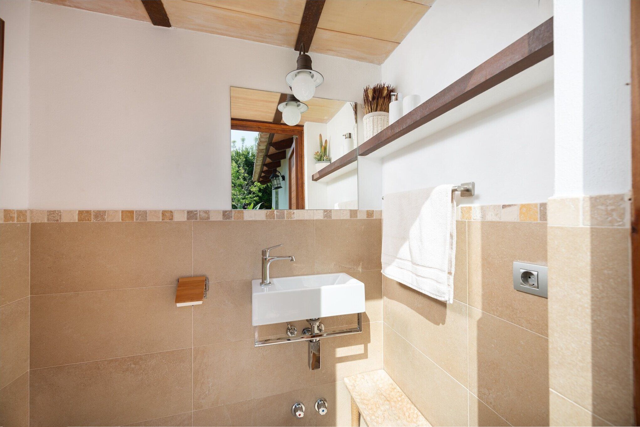 A bathroom with a white sink, wooden shelf, and tiled walls.
