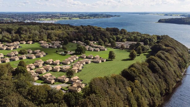 An aerial view of a coastal village with houses arranged in a semi-circular pattern along the shoreline, surrounded by dense greenery and a large body of water. - 6 Person Holiday Park Home in Middelfart (Middelfart)