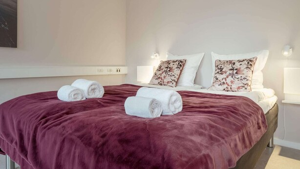 A hotel room with a large bed, two pillows, a red blanket, and two rolled towels on the bed. - 2 Person Holiday Home in Thorshavn (Kjellerup)