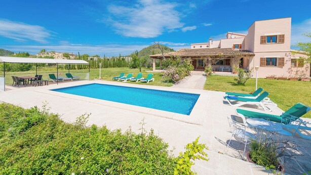Une maison moderne dotée d’une piscine, de fauteuils de jardin verts et d’un patio couvert.