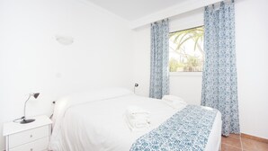Een slaapkamer met een bed, nachtkastje, lamp en een raam met gordijnen.
