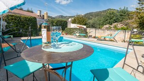 A poolside area with a table, chairs, and a bottle of wine.