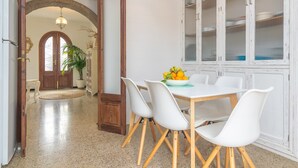 A dining area with a white table and chairs, a bowl of fruit, and a potted plant.