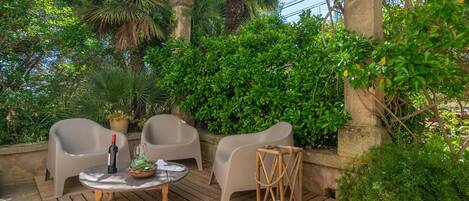An outdoor seating area with two chairs, a small round table, and a bottle of wine.