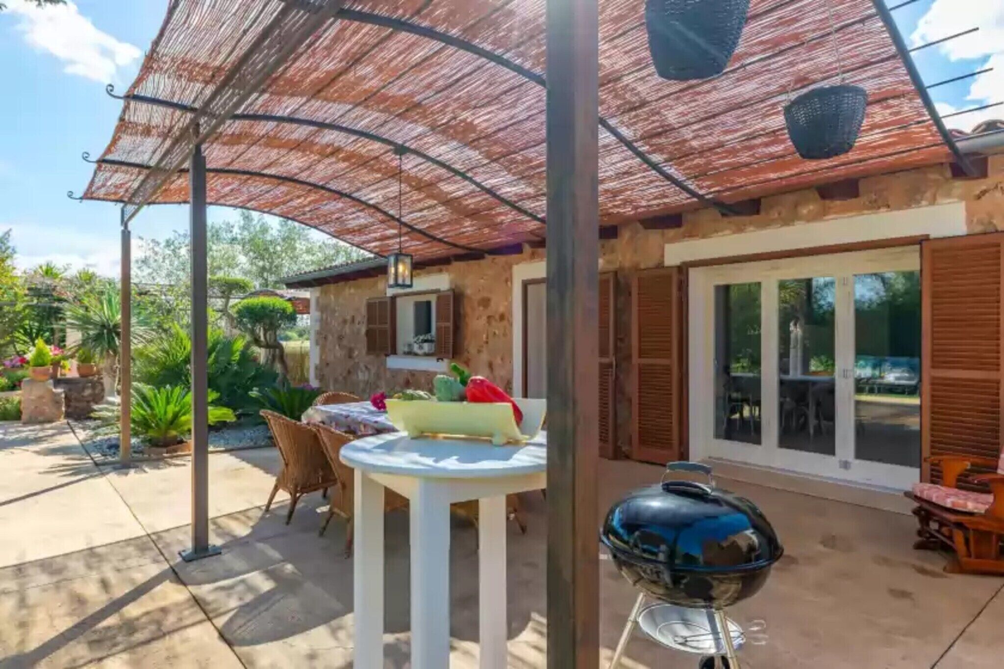 Ein Patio mit Tisch, Stühlen, einem Grill und einer überdachten Sitzgelegenheit mit einem gewebten Sonnensegel.