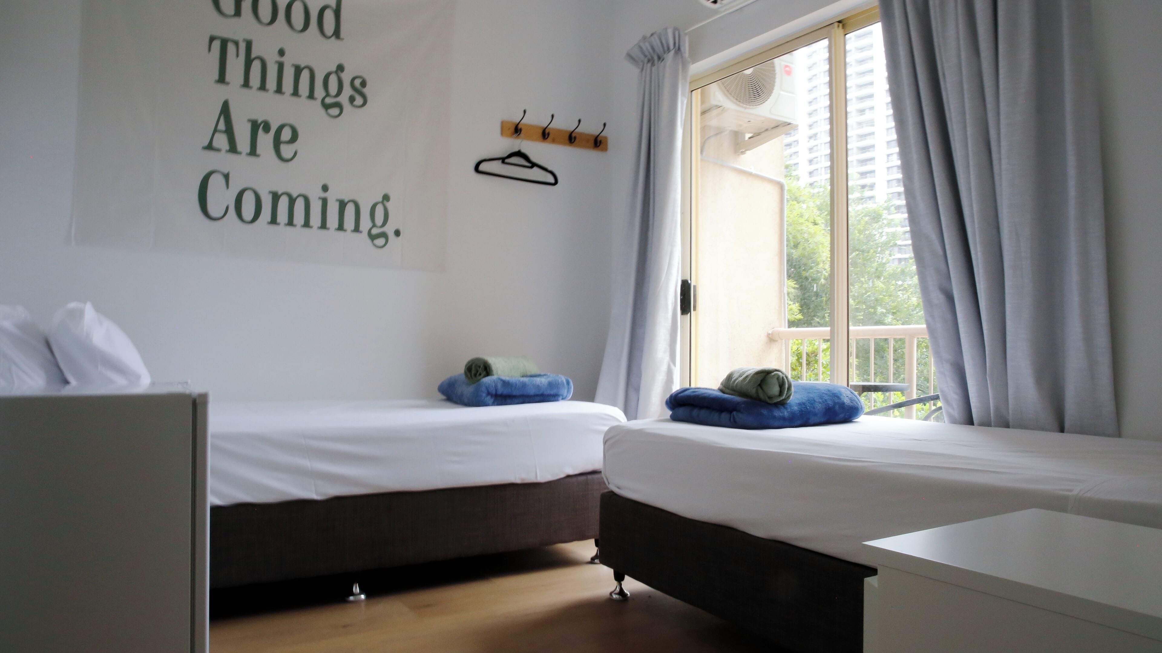 A room with two beds, a wall-mounted coat rack, and a window with curtains.