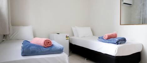 Two single beds with white bedding and rolled towels, a white radiator, and a wall-mounted air conditioner.