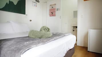 Una cama bien hecha con un edredón gris, una toalla verde y una toalla a rayas colgadas en la pared.