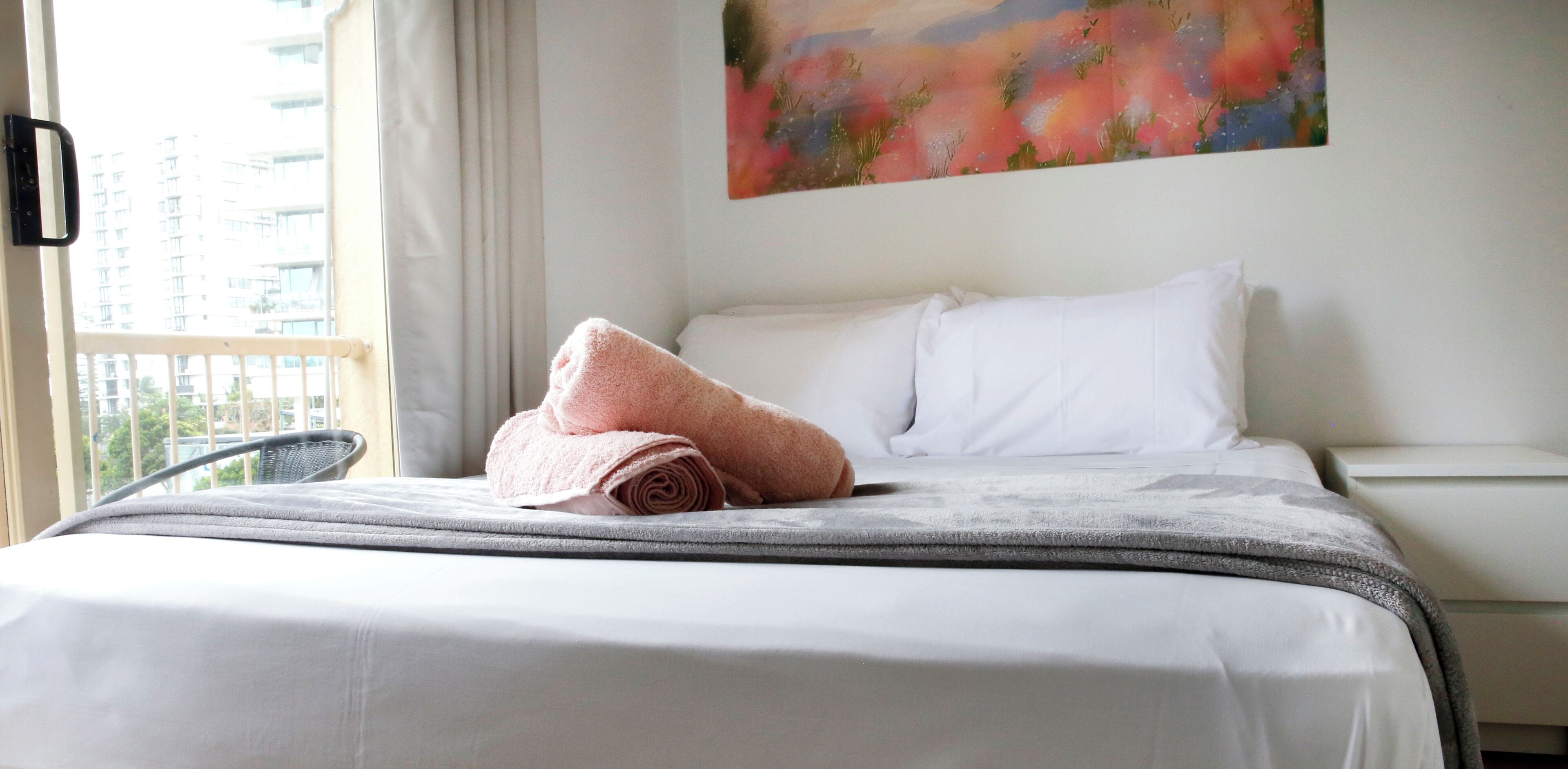 A neatly made bed with a rolled pink towel, white pillows, and a grey blanket.