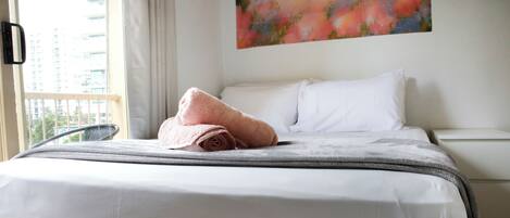 A neatly made bed with a rolled pink towel, white pillows, and a grey blanket.