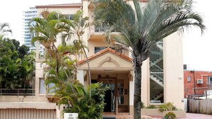 A two-story building with a beige facade, a covered entrance, and a palm tree in the front yard.