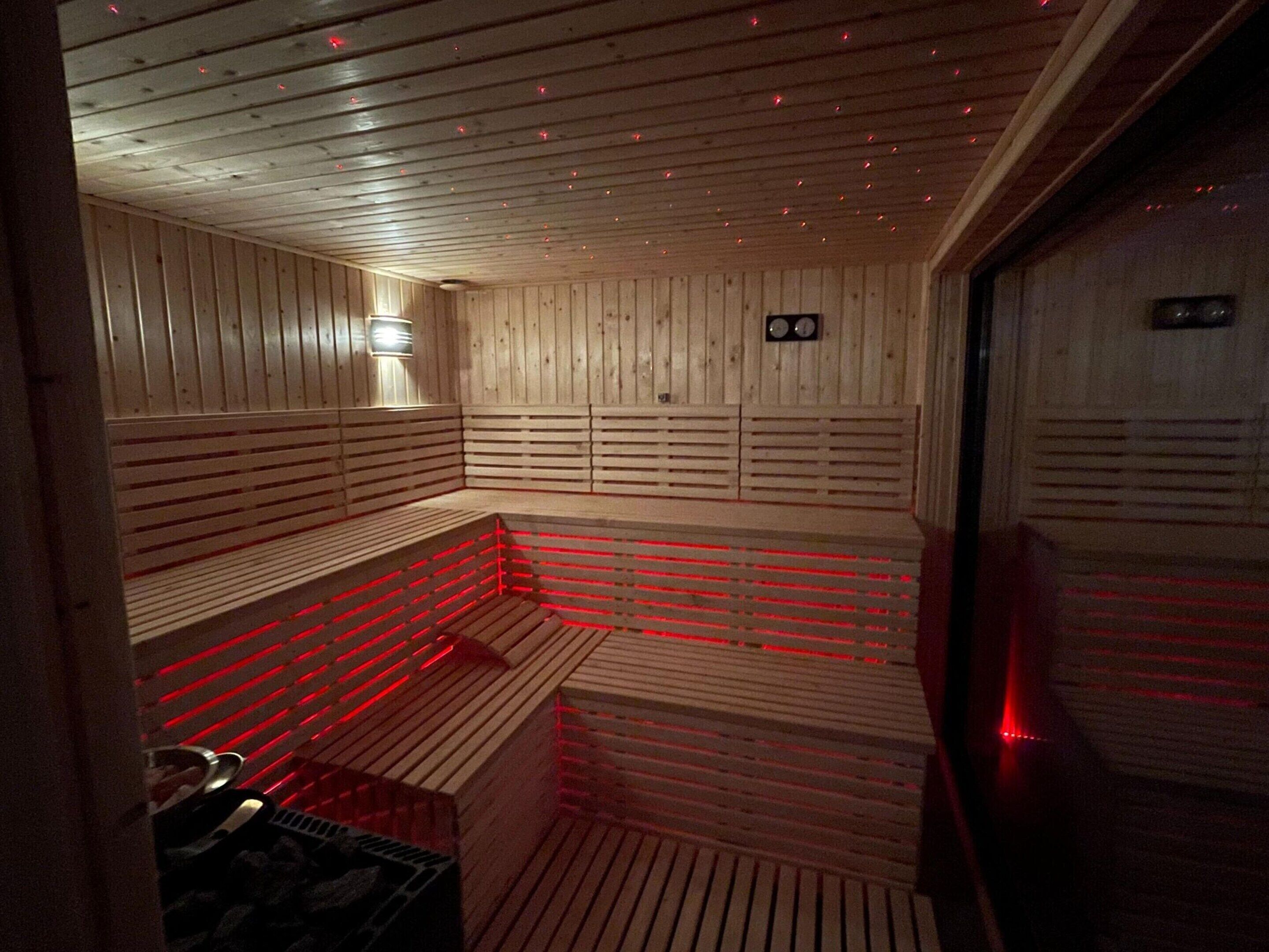 A sauna with wooden benches and slatted walls, equipped with red LED lighting.