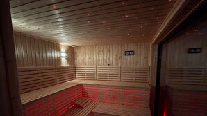 Eine Sauna mit Holzbänken und schmalen Holzlattenwänden, ausgestattet mit roter LED-Beleuchtung.