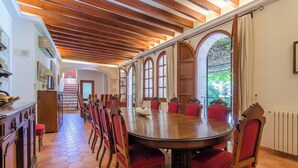 A dining area with a large round table, red upholstered chairs, and a wooden ceiling with exposed beams.