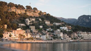 A coastal town with buildings on a hillside, a beach in the foreground, and a calm sea.