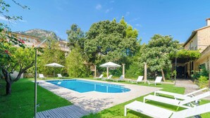 A swimming pool with lounge chairs and umbrellas, surrounded by greenery and buildings.
