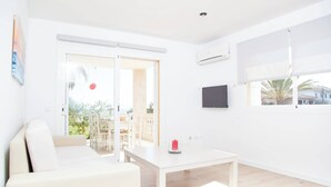 A bright, white room with a sofa, a table, and a TV mounted on the wall. - Sun Of The Bay Vidalba 2 (b2 - A2) - Apartment (Port D'alcudia, Illes Balears)